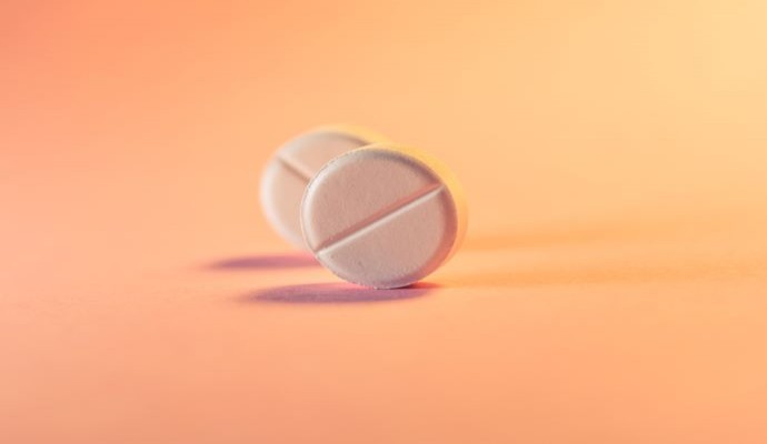 Two white medication tablets against an orange background 