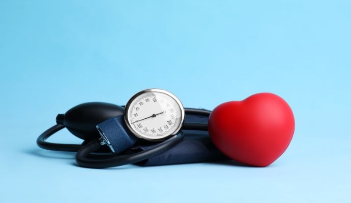 Blood pressure meter and toy heart on light blue background .