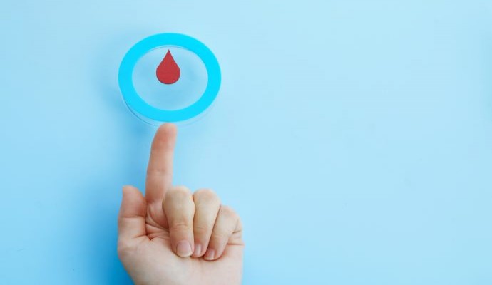 Woman's hand with finger outstretched with a blue circle on the tip and a blood drop in the center, symbolic of the diabetes 