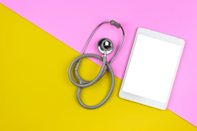 Flat lay of a physician's stethoscope and tablet on pink-yellow background