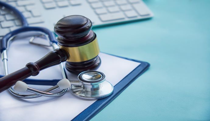 Gavel near stethoscope on file next to a keyboard against a blue background 